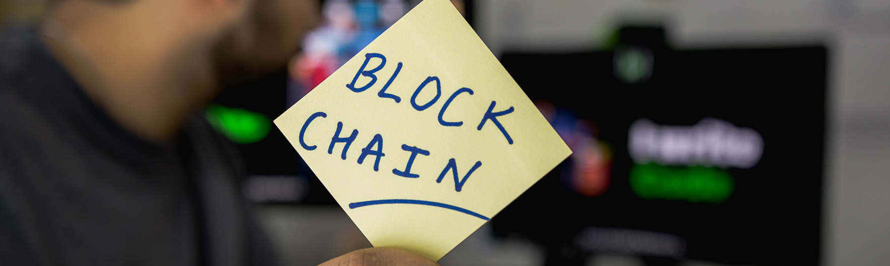 Primeiro plano de um post it com a a palavra "blockchain" escrito em azul